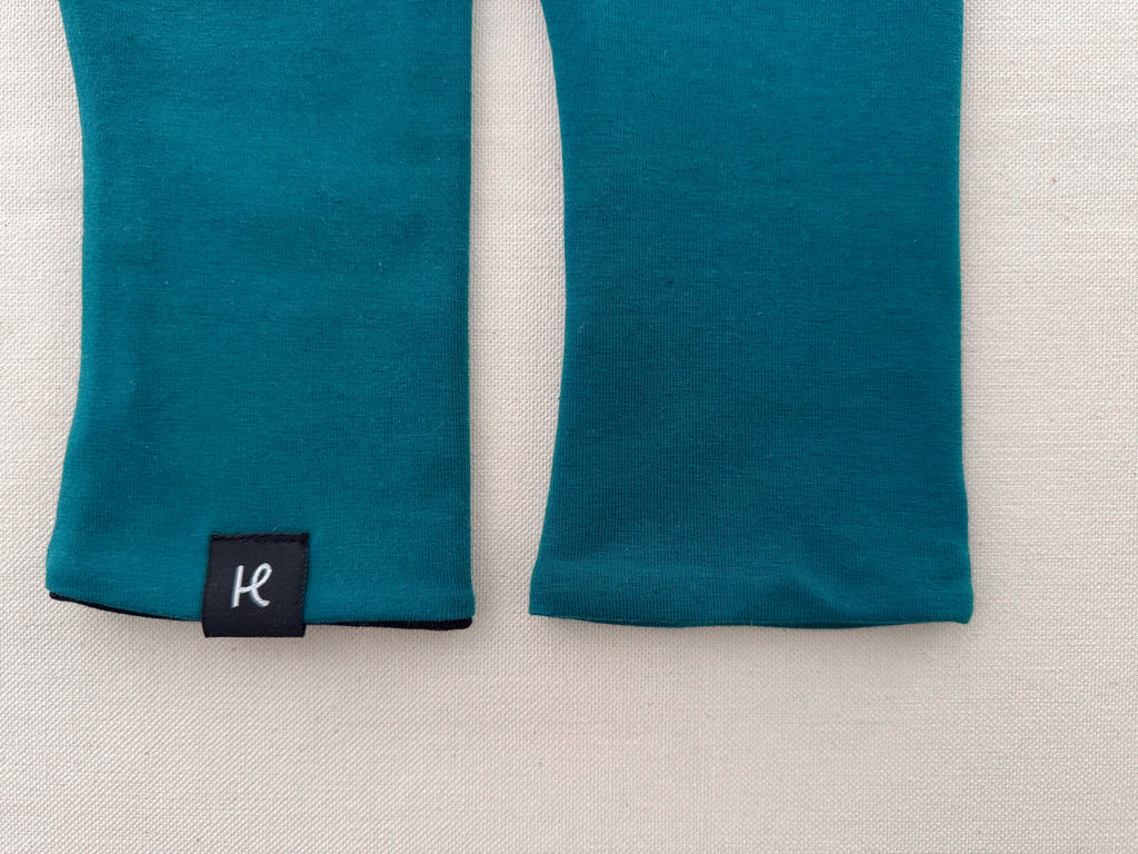 Detalle de etiqueta y logo de los mitones color turquesa de algodón orgánico de Happy Belly