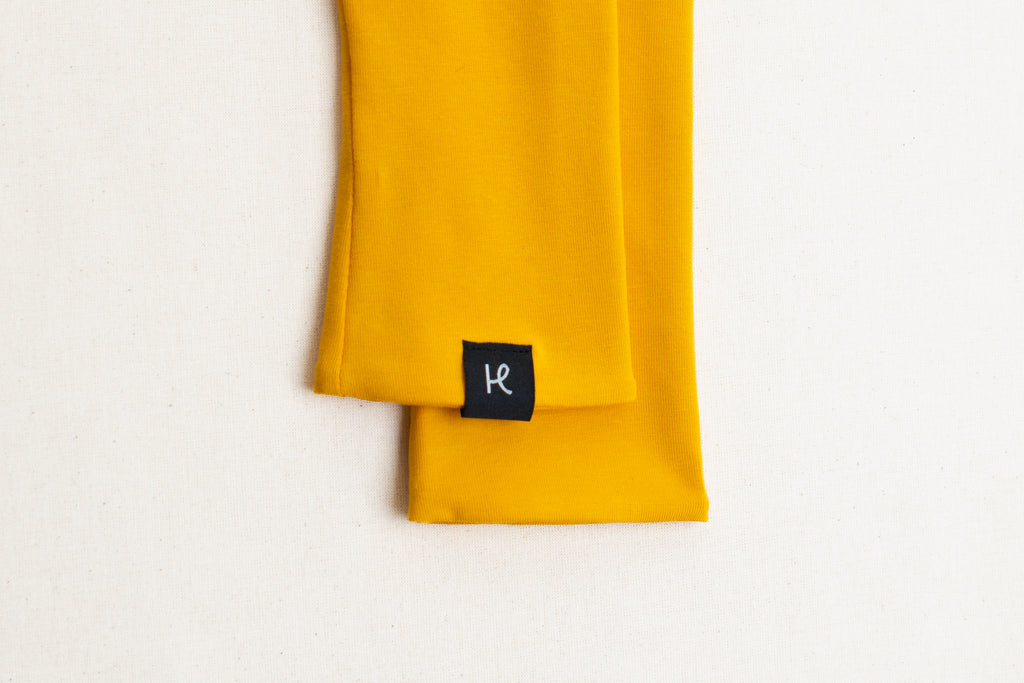 Detalle etiqueta en mitones color amarillo de algodón orgánico, marca Happy Belly