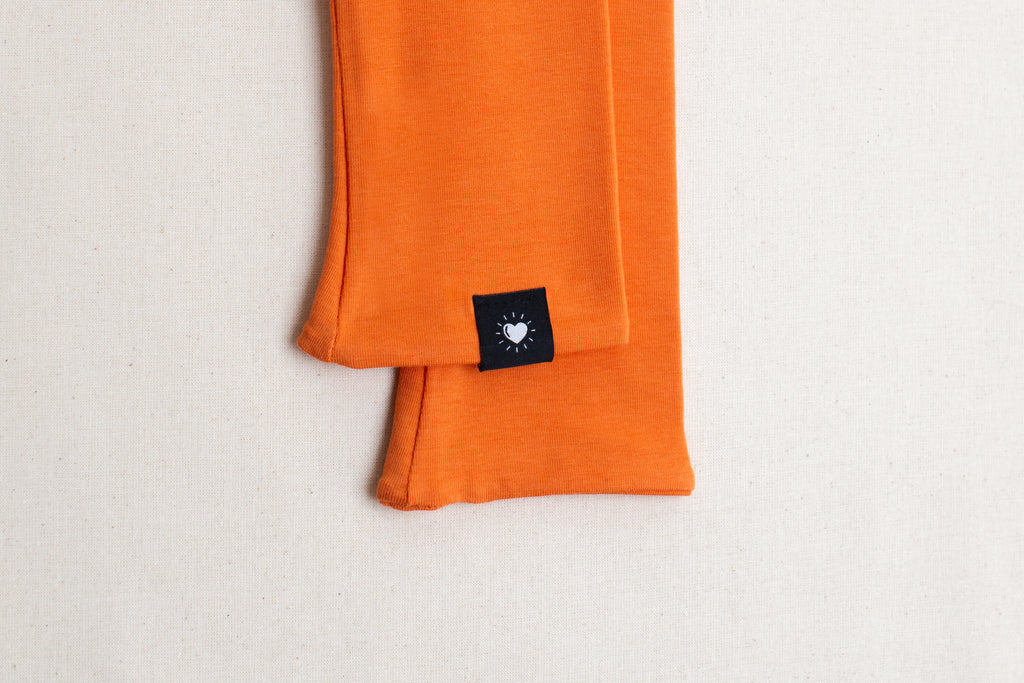 Detalle etiqueta en mitones color naranja de algodón orgánico, marca Happy Belly