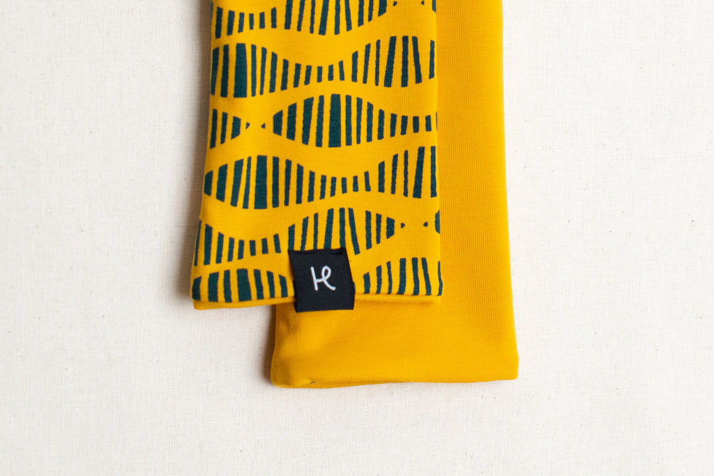 Detalle etiqueta de mitones reversibles en color amarillo estampados con serigrafía artesanal en algodón orgánico